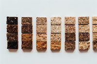 Gradient of chocolate bars arranged in rows showing different cocoa content percentages from dark to milk chocolate on white background, food photography.
