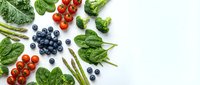Fresh organic vegetables and berries on white background including spinach leaves, cherry tomatoes, broccoli, asparagus and blueberries for healthy eating.