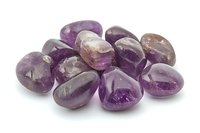 Polished amethyst tumbled stones arranged on white background, showing natural purple crystal variations and smooth surfaces for healing and decoration purposes.