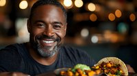 Smiling African American man enjoying delicious taco at restaurant with warm bokeh lights creating cozy dining atmosphere for food and lifestyle content.
