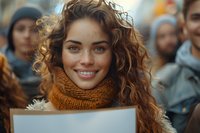 Young Caucasian woman with natural curly brown hair and bright smile wearing cozy orange knit scarf at outdoor public gathering, perfect for lifestyle and activism concepts.