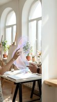 Hands interacting with holographic projection in bright modern workspace with arched windows and plants for futuristic technology presentations.