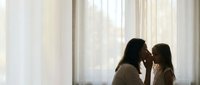 Mother and daughter sharing tender moment by window with soft natural light creating intimate silhouette for family bonding and parenting concepts.
