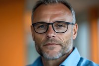 Middle-aged Caucasian businessman with glasses and beard in modern office environment for corporate professional headshot photography.