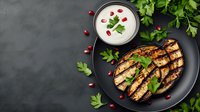 Grilled chicken breast with yogurt sauce and pomegranate seeds on black plate. Fresh parsley garnish creates appetizing contrast. Healthy protein meal.