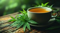 Cup of herbal cannabis tea with fresh marijuana leaves on rustic wooden table against green blurred background, alternative natural medicine concept.