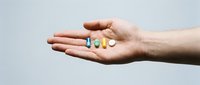 Caucasian hand holding colorful pharmaceutical capsules and pills on neutral background, representing medication, healthcare, vitamins, and wellness treatment options.