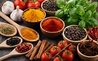 Colorful spices and herbs arranged with fresh vegetables on rustic wooden surface for cooking and culinary preparation.