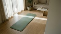 Yoga mat on wooden floor in bright living room with natural light from window, comfortable seating, and potted plant for wellness and fitness training.