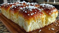 Golden brioche bread rolls with glossy caramelized tops and coarse sea salt crystals on wooden cutting board for bakery and culinary content.