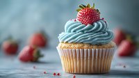 Fresh strawberry cupcake with light blue frosting swirl and ripe berry on top, soft focus background with scattered berries and crumbs on gray surface.