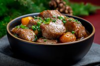Tender braised meat stew with carrots and fresh herbs served in black ceramic bowl on dark background. Traditional homestyle comfort food for winter menu.