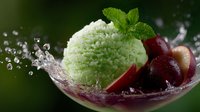 Fresh mint ice cream scoop with red cherries and water splash in glass bowl against dark background, refreshing summer dessert composition.