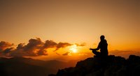 Person meditating on mountain peak during golden sunset with dramatic clouds and warm orange sky creating peaceful spiritual atmosphere.