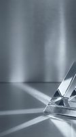 Polished metal geometric shape casting dramatic light rays on reflective surface, creating abstract minimalist composition for modern design projects.
