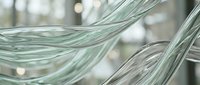 Flowing transparent glass strands intertwine elegantly, creating smooth curves with soft bokeh background in cool green tones.