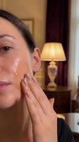 Young Caucasian woman applying facial serum or moisturizer in elegant hotel room for skincare routine and beauty treatment.