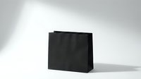 Black paper shopping bag with handles on white background casting soft shadow for retail branding and commercial packaging design mockup.