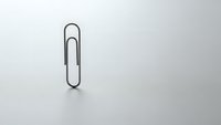 Single black metal paper clip on clean white surface with soft shadow for office supplies and business organization concepts.