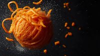 Fresh grated carrot sphere with flying pieces and peels on dark background with water drops, dramatic food photography for healthy eating concept.