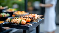 Fresh seafood and meat skewers grilled on black serving platter with blurred restaurant background, selective focus on juicy kebabs with shrimp and vegetables.