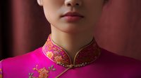 Close up view of traditional Asian pink cheongsam dress with golden embroidered floral pattern and mandarin collar against dark background.
