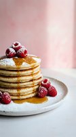 Stack of fluffy pancakes topped with fresh raspberries, maple syrup and powdered sugar on white plate against soft pink background for breakfast menu.