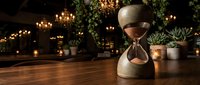 Vintage hourglass on wooden table with warm lighting and plants creating cozy atmospheric scene for time management and productivity concepts.