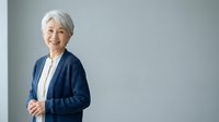 Senior woman with gray hair wearing navy cardigan and white shirt, standing against neutral background, suitable for corporate, healthcare, and lifestyle marketing materials.