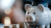 White ceramic piggy bank with coins on table representing savings and financial planning for future investment goals.