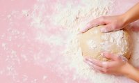 Female hands kneading raw dough on pink background with scattered flour. Homemade baking process captured from above showing pastry preparation.