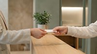 Two people exchanging blank business cards at wooden desk in modern office setting, wearing light striped shirts, professional networking and corporate communication concept.