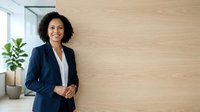 Professional woman with curly dark hair and medium skin tone wearing navy blazer and white shirt, standing confidently in modern office with potted plant, suitable for corporate and business content.