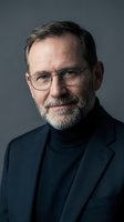 Middle-aged man with gray beard and glasses wearing dark blazer and turtleneck against neutral background for corporate, professional, and business portrait use.