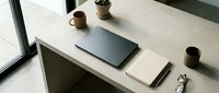 Minimalist workspace with laptop, smartphone, and potted plants on white desk near window for modern office design projects.