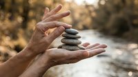 Hands carefully balancing stack of smooth river stones in peaceful outdoor setting, symbolizing harmony, mindfulness and zen meditation practice.