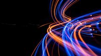 Dynamic light trails creating swirling motion patterns in blue and orange colors against black background for modern digital design projects.
