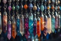Colorful crystal pendants and gemstone points hanging on chains, featuring amethyst, quartz, and other minerals in vibrant hues against dark background.