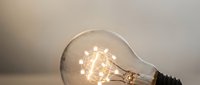 Glowing vintage incandescent light bulb with visible filament against soft neutral background creating warm ambient lighting for creative projects.