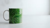 White ceramic mug with green circuit board pattern design for tech enthusiasts and electronics professionals in modern office setting.