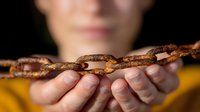 Rusty metal chain held in hands against dark background, symbolizing connection, bondage, strength and industrial concepts. Close up view with selective focus.