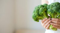 Fresh green broccoli florets held in hands against neutral background, showcasing healthy organic vegetables for cooking, nutrition, and wellness content.