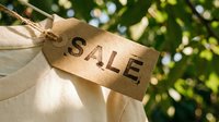 Kraft paper sale tag tied to white clothing with green foliage background, eco-friendly retail discount concept for seasonal promotions.