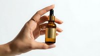 Female hand holding amber glass dropper bottle with golden serum oil for skincare routine and beauty treatment on white background.