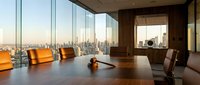 Modern executive boardroom with panoramic city skyline view through floor-to-ceiling windows, featuring sleek conference table and leather chairs.