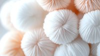 Soft white fluffy pompoms in gentle peach and cream colors create delicate textural background pattern for design, crafts, and decorative projects.