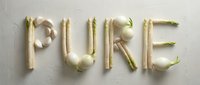 Word PURE spelled with fresh white vegetables including asparagus, garlic, and onions on a light textured background, healthy food concept.