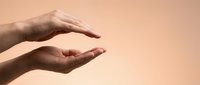 Two hands creating protective gesture against warm beige background symbolizing care, safety, security and support for insurance or healthcare concepts.