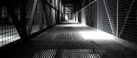 Industrial metal walkway with geometric shadows and dramatic lighting creating perspective tunnel effect in modern architectural structure.