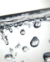 Macro photography of water drops falling and splashing, creating crystalline spheres and abstract formations against white background. Pure liquid dynamics in motion.
